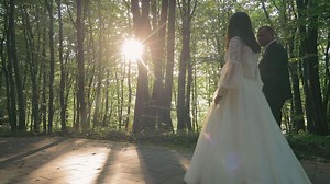Wedding couple walking through a sunlit forest. A bride and groom walk through a peaceful forest with sunlight streaming through the trees.
