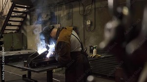 Blacksmith welder in protective mask works with metal using a welding machine, bright sparks. 4K flat footage