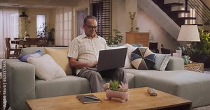 Elderly Indian Man Using Laptop at Home: Using Online Platforms to Explore His Interests, Delving into History, Arts, and Literature. Cultivating Wisdom and Sharing Stories On Social Media. Wide Shot