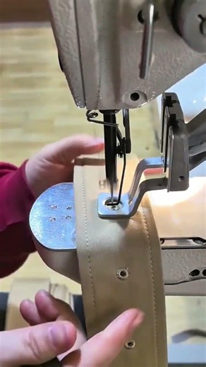 sewing round metal eyelets on a tan fabric strap using a sewing machine for professional production