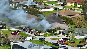 Burning residential house on fire with smoke and flames and firefighters extinguishing it after short circuit spark ignited wooden roof damaged by hurricane. Home disaster in Florida rural area