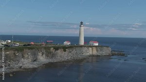 The Scenic Cap-Des-Rosiers Lighthouse Near The Village Of Cap-Des-Rosiers In Gaspe, Quebec, Canada On A Sunny Day - wide drone shot, orbiting