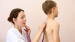 doctor listens to back of boy putting diaphragm of stethoscope