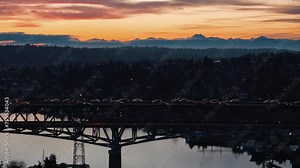 Cars drive across the I5 highway bridge in Seattle over Lake Union while the sun sets behind the Olympic Mountains