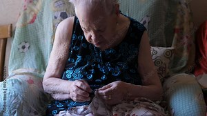 A 90-year-old woman mends a torn sweater, showcasing her skill and patience in repairing clothing. This close-up highlights the meticulous process of mending.
