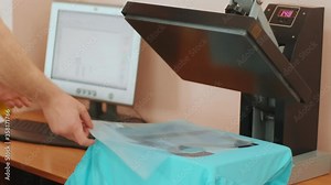 Heat press machine with t-shirt on wooden table. Worker presses a hand press to apply numbers to a high temperature T-shirt