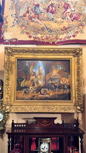 A captivating blend of artistry and mechanical ingenuity, this French animated musical painting clock transforms a telling time into a theatrical scene. The finely painted composition depicts the bustling interior of a rural blacksmith’s workshop beneath vaulted arches. At the left, a farrier fits a horseshoe with the help of a rider as a small dog looks on, while on the right several smiths work together at the forge. Through the archway, a picturesque village street leads the eye toward a dist