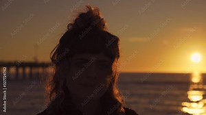 Slow motion of a young model woman brunette girl with a fringe and a braid at Venice Beach in Florida by the golden light of the evening sun by sunset making eye contact and waves moving.