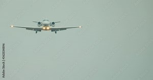 A light plane lands at the airport. The plane with the light on flies over the frame against the blue sky.