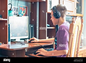 A teenage boy, a young man playing video games on a computer, using technology, wearing headphones, using a computer.A young man, a teenager using tec Stock Photo - Alamy