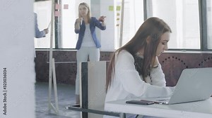 Woman manager in a business suit draws charts on a glass board. Nearby are the project managers and help her solve the problem. The camera slides slowly