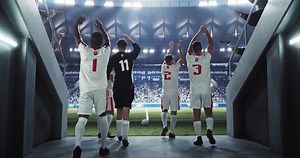Soccer Players Walking Through a Dark Tunnel Entrance to a Big Outdoors Stadium Filled with Energetic Sports Fans and Team Supporters. Multiethnic Footballers Warming Up Before a Match