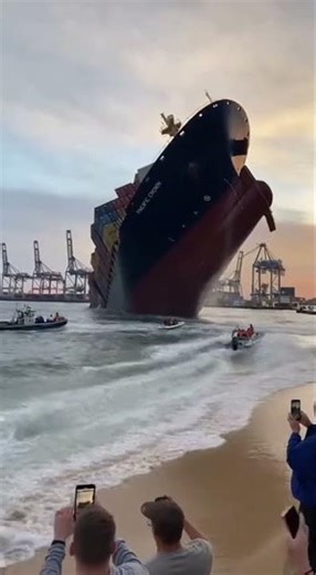 A massive ship begins sinking near a busy harbor while nearby boats keep their distance and people