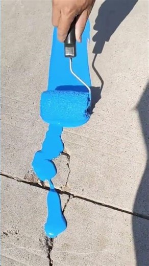 Man applying vibrant blue paint over concrete cracks with roller