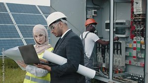 Male and female inspectors with laptop and papers standing talking on field with solar panels. African american technician standing behind near switchgear and showing thumb up on camera