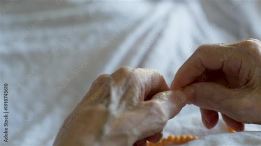 Elderly Hands with Prayer Beads. Close-up of a senior person's weathered hands holding amber prayer beads while in bed. Concept of faith, aging, spirituality, and home healthcare