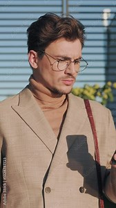 Portrait of handsome man in glasses use phone look around stand near car on street. Good looking guy scrolling social media. Slow motion