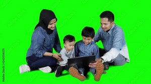Happy casual family using a laptop computer while sitting on the floor in the studio. Shot in 4k resolution with green screen background