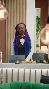 Vertical video Hotel concierge greeting tourists at five star resort, talking to clients for check in process to review online room booking. African american people travelling with luggage, arriving