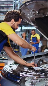 Vertical video Qualified serviceman in car service picks torque wrench from work station bench, using it to tighten bolts after replacing engine. Garage worker fixes client automobile, jib down shot