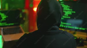 Hacker writing code cracking computer. Man programmer in hoodie cracks system, using computer in dark room back view. Hacker attack, technology, virus infected software, cyber man hacker concept.