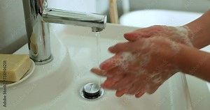 Coronavirus pandemic prevention washing hands rubbing wrist and palms with fingers interlaced. Woman using correct handwashing technique at sink in bathroom at home. Female hands hand washing closeup.