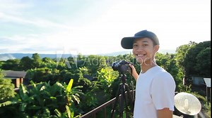 Happy yong asian man with camera gear smiling while take a photo of village landscape, Beginer of young photographer training photography course at outdoor workshop.