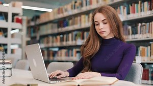 Female student works with books and a laptop sitting at the table in the library