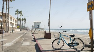 Blue bicycle, cruiser bike by ocean beach, pacific coast, Oceanside California USA. Summertime vacations, sea shore. Vintage cycle by road sign. Palms, lifeguard tower watchtower hut. Pelicans flying.