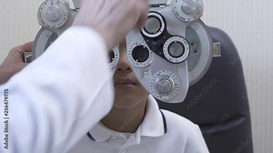 Little boy's eye examination at optometrist ophthalmologist using phoropter close up. Hands of doctor in white medical coat puts phoropter to eyes of teen boy. Slow motion.