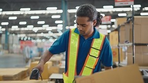 Warehouse worker using a QR code reader, scanning parcels into the system while working inside a large distribution center, worker checking goods packages and making inventory of goods.