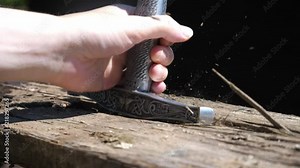 Close up shot of a sword being driven through an old wooden plank. The hilt reaches the base of the wood and shocks particles into the air. Slow mo Stock Video