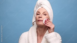 Attractive middle-aged, mature woman taking care after skin, applying face toner against blue studio studio background. Concept of natural beauty, face skin care, cosmetics