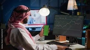 Remote worker holding green screen smartphone while looking at business annual report graphs on computer. Self employed freelancer with mockup phone in hand performing tasks on device