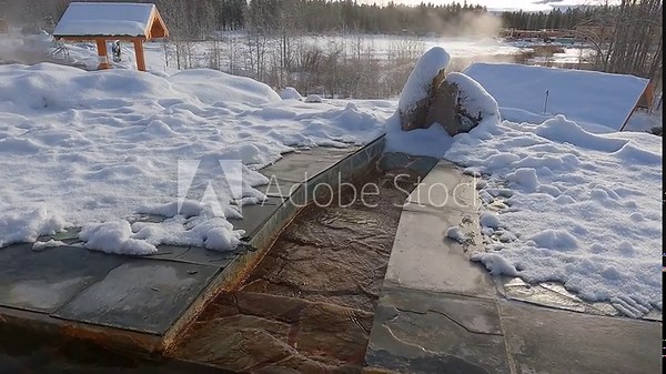 A stationary shot of a stream of warm, iron-rich mineral water flowing through a snow-covered flagstone channel at the nordic hot springs near Whitehorse, Yukon