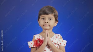 young girl kid on blue background doing namaste by looking camera - Concept of respectful greetings or saying hi or hello in indin culture