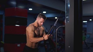 Athletic guy pumping his muscles. Shirtless bodybuilder training his sportive body in the gym. Side view. Sportive lifestyle.