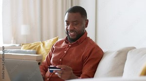 Positive african american guy entering credit card data on website, making payment on laptop, tracking shot, free space
