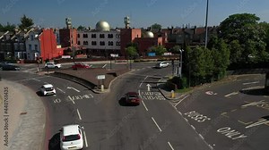 Car driving on Lea bridge roundabout, Madina Mosque Trust building behind road.