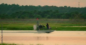 An airboat glides through a central Florida swamp and grassy wetlands in search of wildlife viewing and gator hunting at sunset. Slow motion.