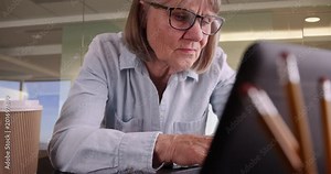 Close-up of senior woman typing on laptop working in corporate workplace, Portrait of older woman using portable computer in modern office space setting, 4k
