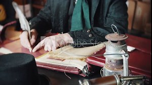 Victorian Scrooge in a counting house shop bookkeeping. Features weighing scales, ledger book & top hat. The gentleman is dressed in jacket, shirt and velvet tie. He is writing with a feather quill.