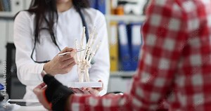 Doctor holds model of skeleton of the hand and patient with hand injury