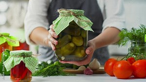 Cucumber pickle An active housewife holds a glass jar with fermented vegetables in her hands. The process of preserving vegetables is a way to preserve food in a marinade for a long time.