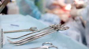 Close-up of surgical instruments in use during an operation, set against the backdrop of a busy operating room. This photo highlights the precision and essential tools involved in a medical procedure.
