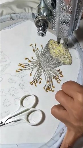 embroidering a gold and silver floral pattern on white fabric using a professional sewing machine