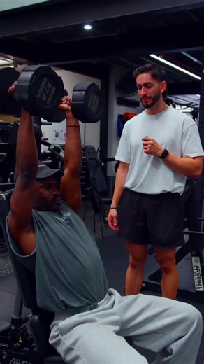 Seated vs. Standing: Choosing Your Overhead Press The choice between seated and standing variations changes the mechanical load on your joints and determines whether you are prioritising hypertrophy or functional stability. The Seated Press: Maximum Isolation - A seated press with back support stabilises the pelvis and spine, allowing for: - Higher Mechanical Tension: Removing the balance requirement lets you move heavier loads, making it superior for deltoid growth. - Scapular Fixation: The ben