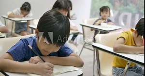 School boy writing on his notebook, taking exam in the classroom.