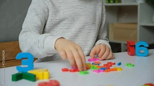 Preschool or primary school child putting together math examples from plastic numbers while sitting at table. Stock Video