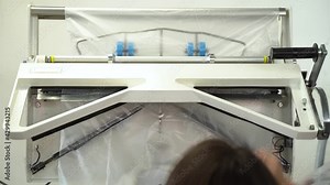 Close-up of men's suit jacket hanging during packing in polyethylene after dry-cleaning in salon. Special equipment packing clean clothes on hangers at the end of professional dry cleaning